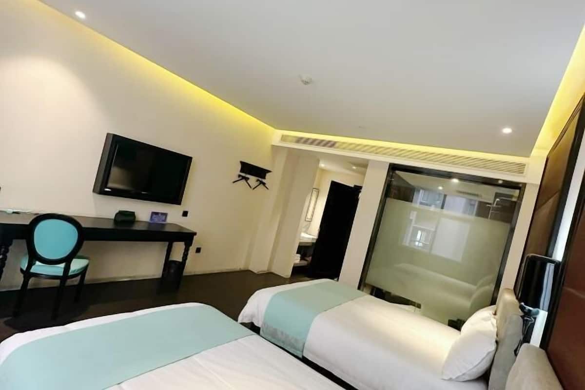 Habitación de hotel con dos camas, un escritorio, una silla, un televisor y un separador de vidrio.