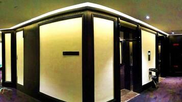 A hotel lobby with a modern design, featuring a large, illuminated reception desk and a carpeted floor.