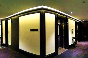 A hotel lobby with a modern design, featuring a large, illuminated reception desk and a carpeted floor.