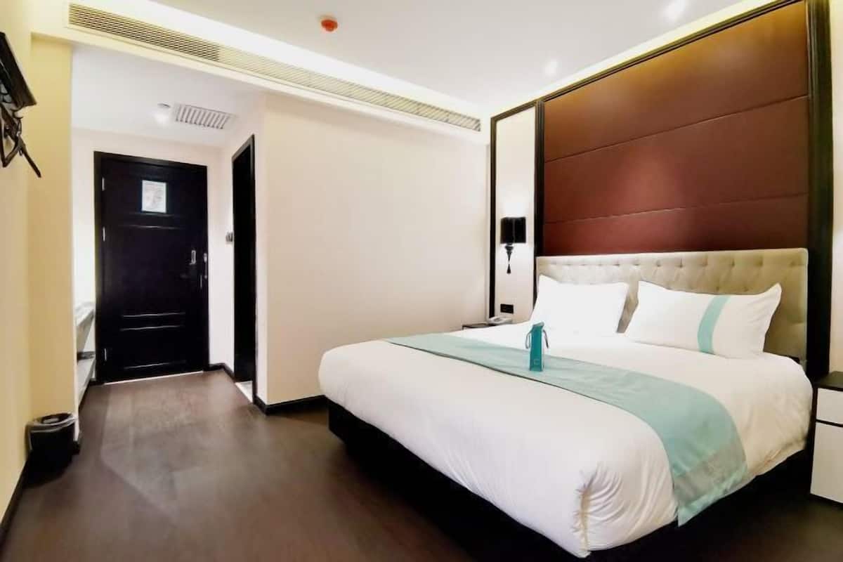 Una habitación de hotel con una cama grande, una mesita de noche, una lámpara y una puerta.