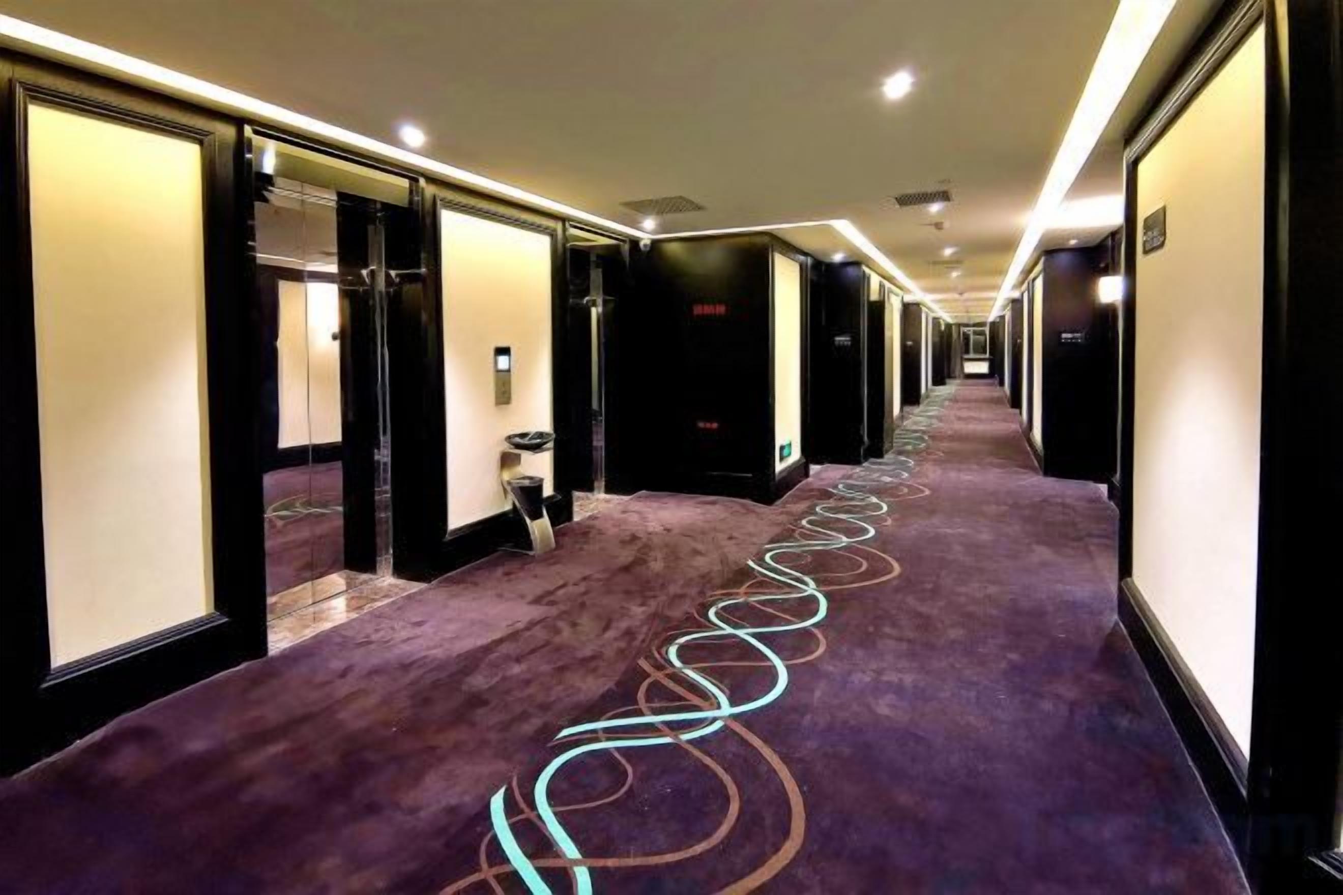 A hotel corridor with a purple carpet, doors on both sides, and a long hallway.