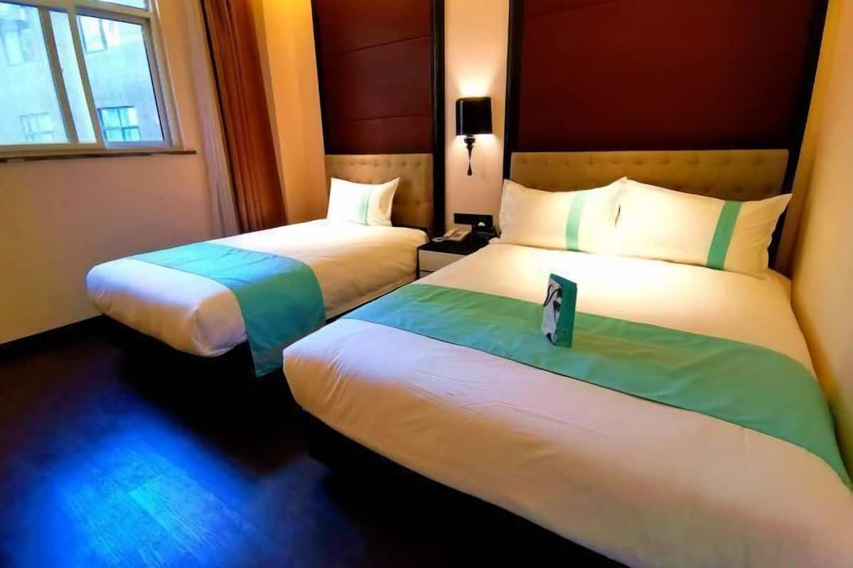 Habitación de hotel con dos camas, una mesita de noche, una lámpara y una ventana con cortinas.