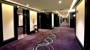 Un couloir d’hôtel avec un tapis, des portes et un long couloir, le tout dans des tons violets.
