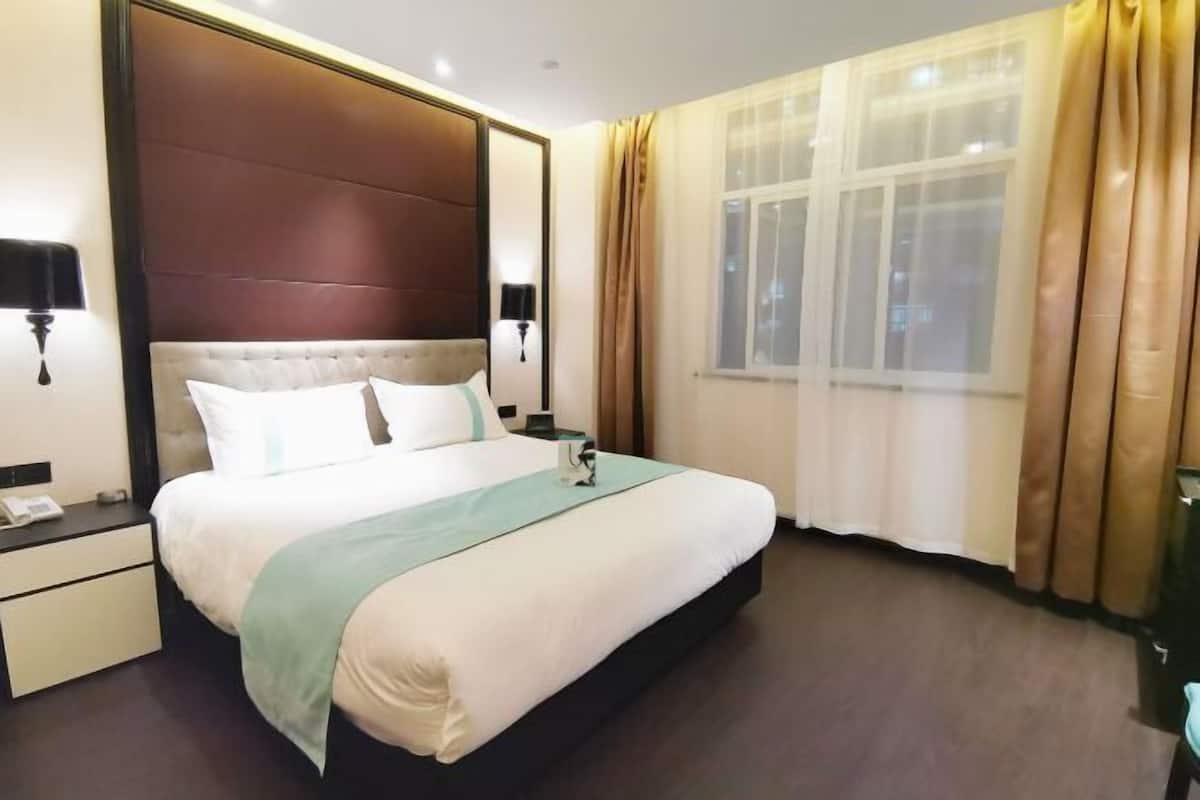 Habitación de hotel con una cama grande, una mesita de noche, una lámpara y un ventanal con cortinas.