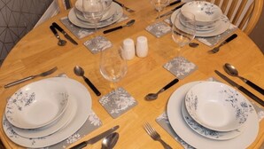 Una mesa redonda para comer dispuesta con platos, vasos, cubiertos y saleros y pimenteros.