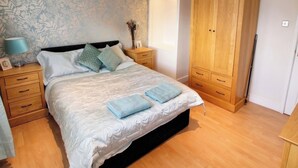 Un dormitorio con cama, mesitas de noche, un armario y un papel tapiz con motivos florales.