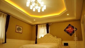A bedroom with a large bed, a bedside table, a nightstand, a wall-mounted lamp, and a ceiling light fixture.