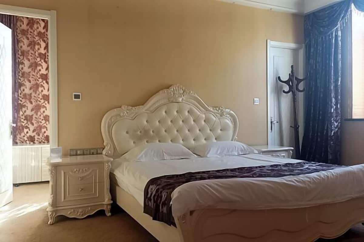Une chambre à coucher avec un grand lit, une table de chevet, une commode et une fenêtre avec des rideaux.