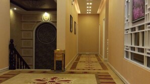 A hallway with a carpeted floor, a staircase, and a wall-mounted light fixture.