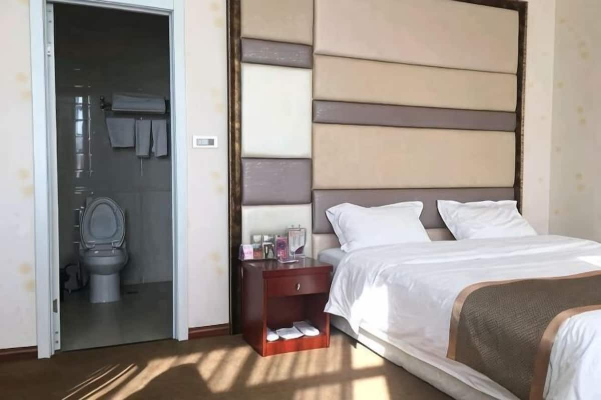 Une chambre d’hôtel avec un lit, une table de chevet, une salle de bain visible à travers une porte ouverte et une tête de lit fixée au mur.