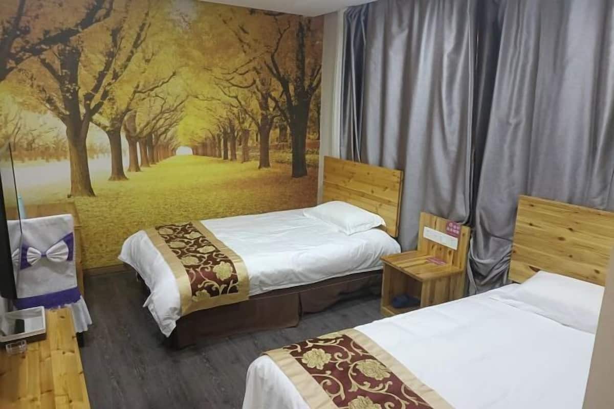 Une chambre d’hôtel avec deux lits, une tête de lit en bois, une petite table de chevet en bois, un miroir et une grande fresque murale représentant un sentier forestier.