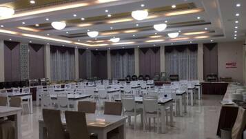 A banquet hall with multiple tables and chairs, a stage, and a long counter.