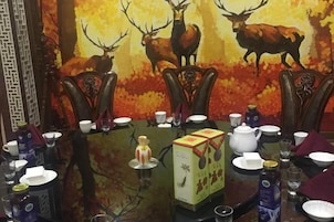 Una mesa de comedor dispuesta con sillas, una caja de té y un cuadro de ciervos al fondo.