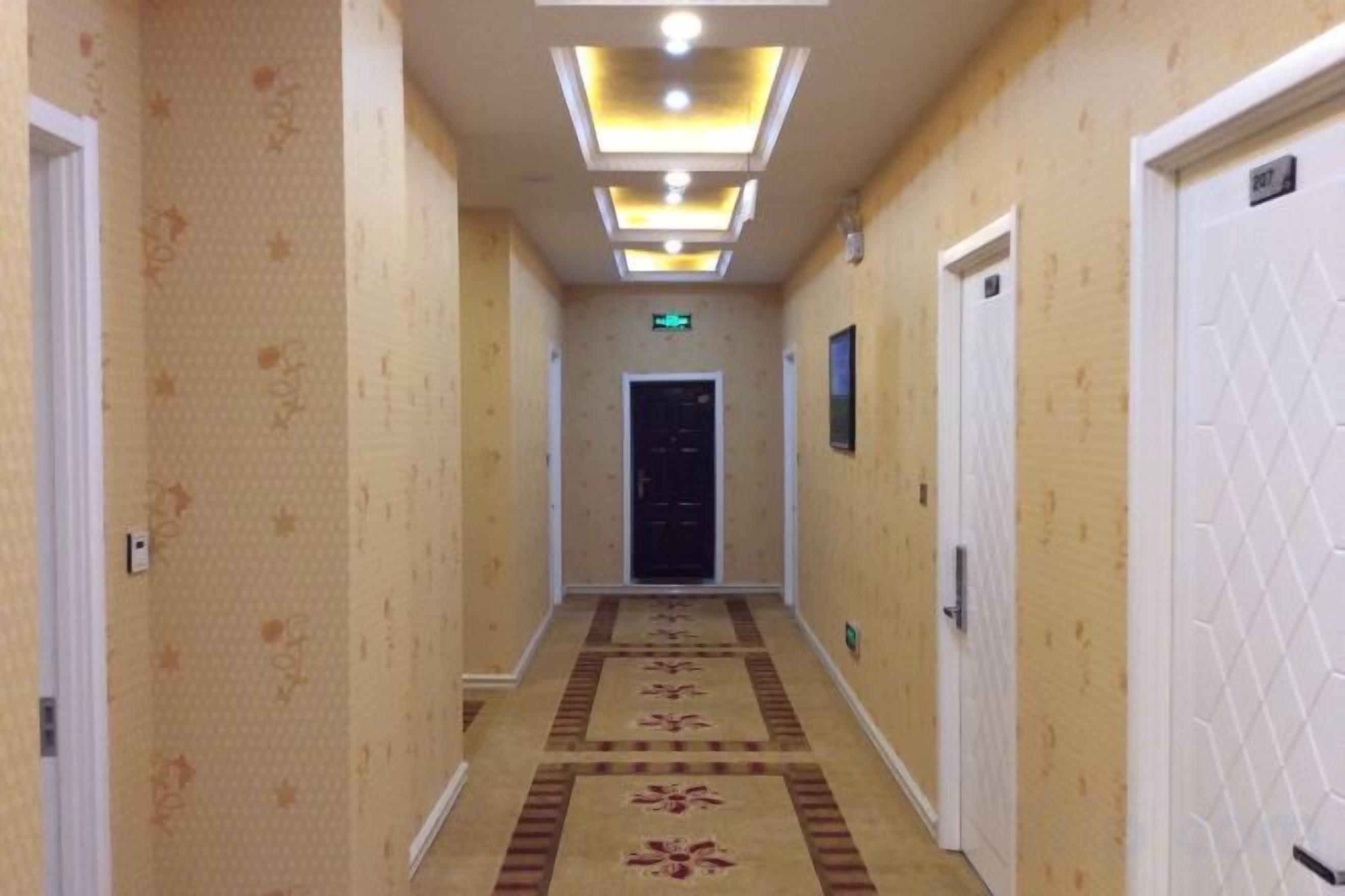 A hotel hallway with carpeted flooring, doors on both sides, and a ceiling with recessed lighting.