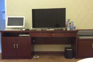 Habitación de hotel con un escritorio de madera, un televisor, un monitor y un bote de basura.