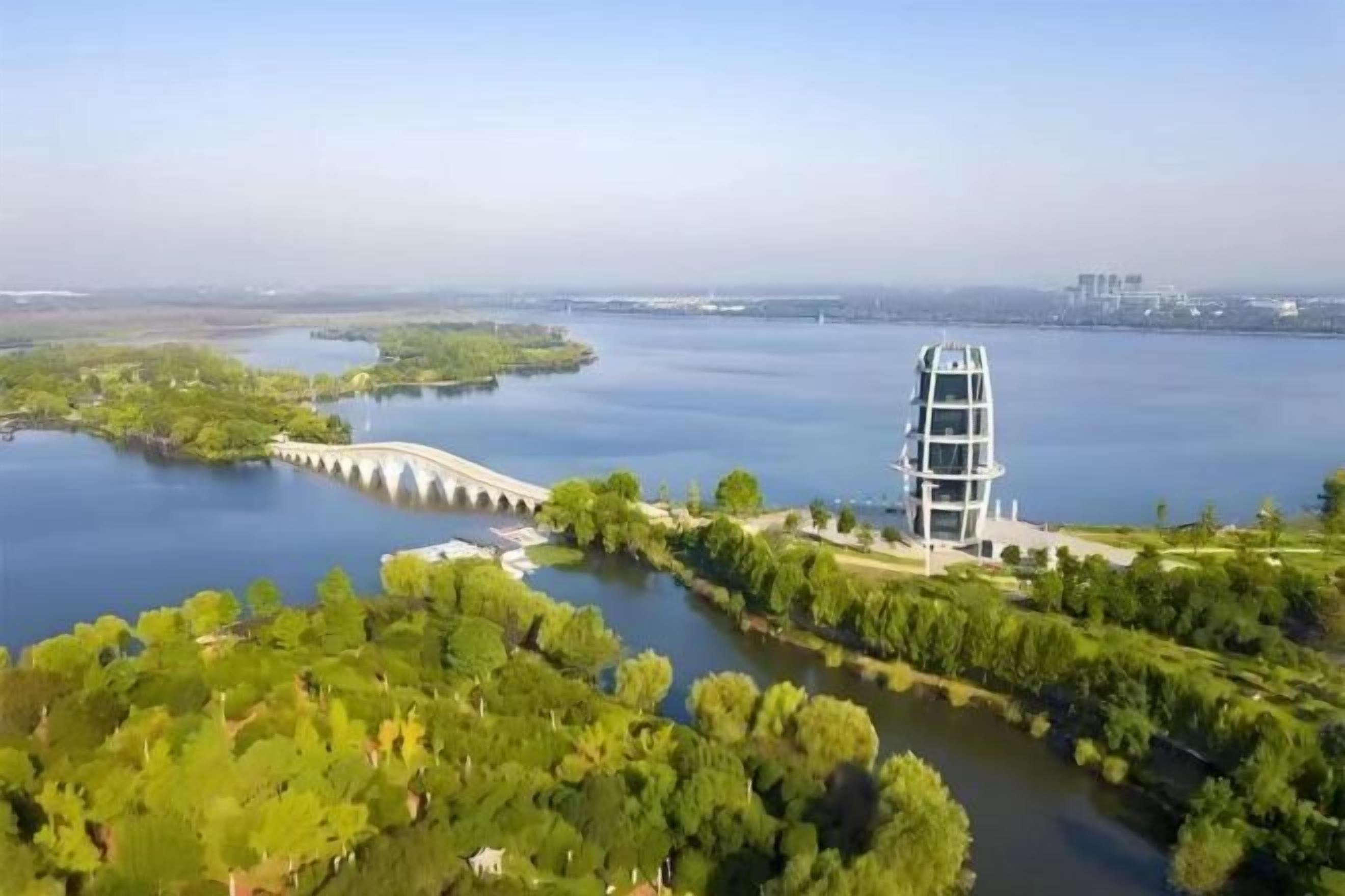 A modern building with a unique architectural design, surrounded by lush greenery and a calm body of water.