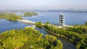 A modern building with a unique architectural design, surrounded by lush greenery and a calm body of water. - China Inn (Donghai Xingfu Bridge) (Donghai)