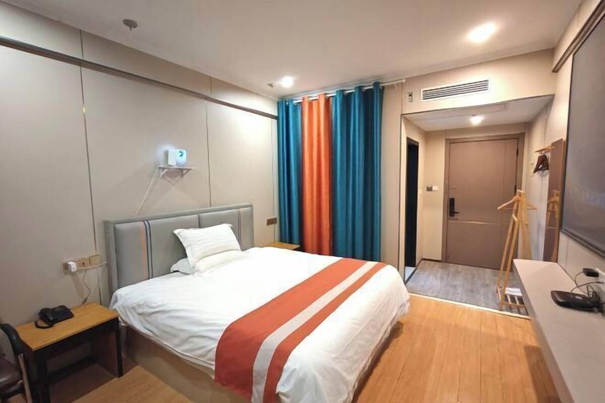 A hotel room with a bed, a desk, a chair, a wardrobe, a mirror, and a door.