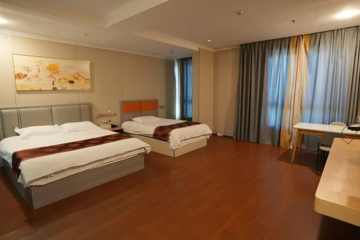 A hotel room with two beds, a desk, and a large window with curtains.
