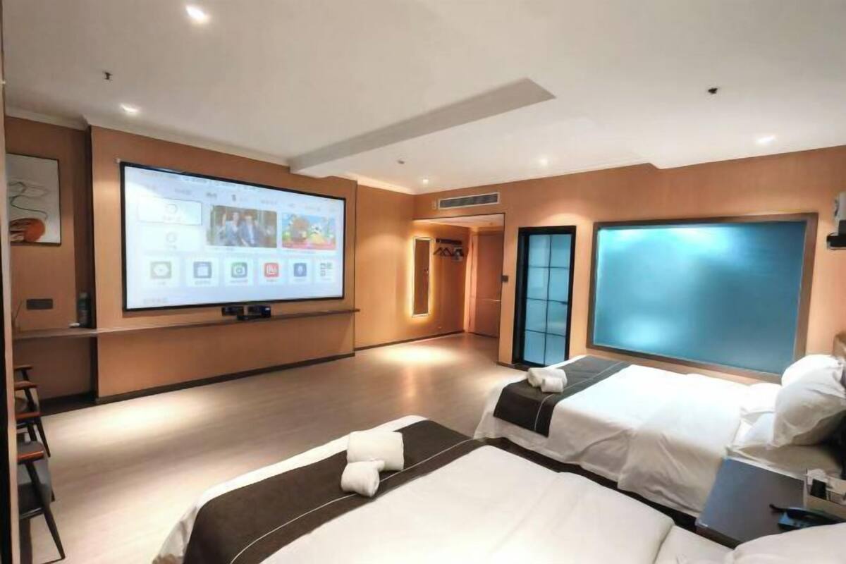 A hotel room with two beds, a large screen, and a view of the city.