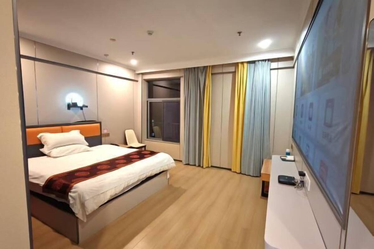 A hotel room with a bed, a TV, a desk, and a window with curtains.