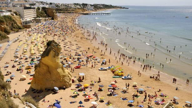 Una playa concurrida, con bastantes sombrillas y gente disfrutando del mar.