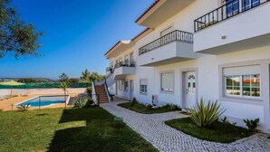 Una casa de varios pisos con piscina, un camino pavimentado y vistas al mar.
