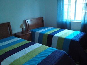 Une chambre avec deux lits, une table de chevet, une lampe et une fenêtre avec des rideaux.