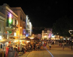 Une rue animée de nuit, avec des boutiques et des passants.