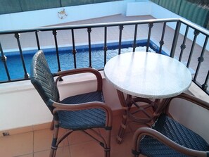 Un balcon avec une table ronde et deux chaises en osier, donnant sur une piscine.
