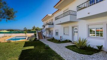 Uma casa de vários andares com piscina, um caminho pavimentado e vista para o mar.