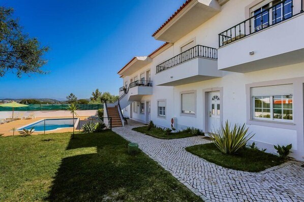 Une maison à plusieurs étages avec une piscine, un chemin pavé et une vue sur la mer.