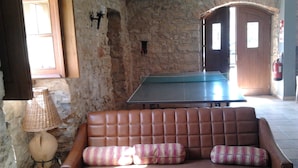 A stone-walled room with a brown leather sofa, a table tennis table, and a lamp. - Historical 4 - Bedroom Villa in Alcobaca (Alcobaca)
