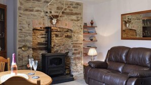 A cozy living room with a stone fireplace, a leather sofa, and a small table with a bottle and glass. - 1 Bed House - Garden, Parking, Pets Allowed (Lynton)