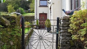 A cottage entrance with a metal gate, a stone wall, and a bird perched on the wall. - 1 Bed House - Garden, Parking, Pets Allowed (Lynton)