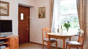 A room with a wooden door, a television on a stand, a table with chairs, and a window with curtains. - 1 Bed House - Garden, Parking, Pets Allowed (Lynton)