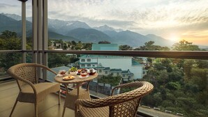 A balcony with wicker furniture and a table set for tea, overlooking a mountainous landscape with buildings in the background. - Infinitea Centric Dharamshala (Dharamshala)