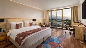 A hotel room with a large bed, a desk, a chair, and a view of mountains through a large window. - Infinitea Centric Dharamshala (Dharamshala)