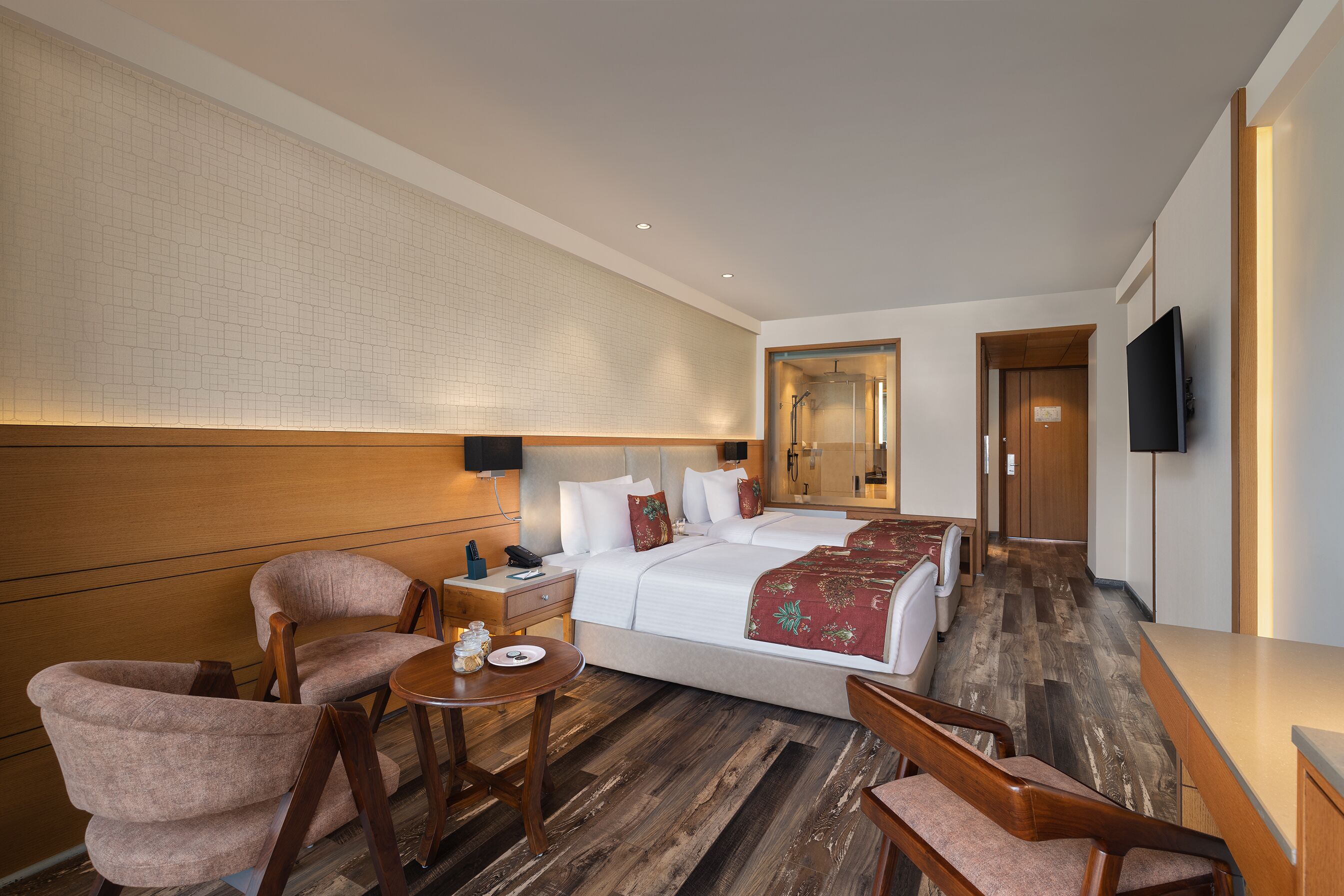 Een hotelkamer met een groot bed, een bureau, twee fauteuils, een bijzettafeltje en een televisie.