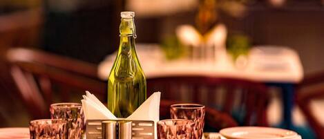 Una mesa de comedor dispuesta con platos, vasos y una botella, rodeada de sillas.