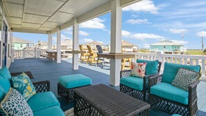 A covered outdoor seating area with wicker furniture and teal cushions, overlooking a residential area with houses and a clear sky. -  Private Heated Pool & Hot Tub ~ Ocean View ~ King Beds ~ Quiet & Peaceful (Bolivar Peninsula)