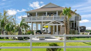 A two-story house with a balcony, surrounded by a white fence and palm trees. -  Private Heated Pool & Hot Tub ~ Ocean View ~ King Beds ~ Quiet & Peaceful (Bolivar Peninsula)
