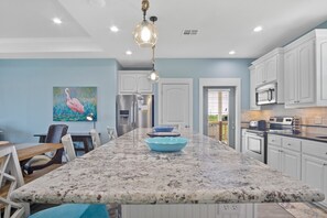 A kitchen with a granite island, white cabinets, and a painting of a flamingo.