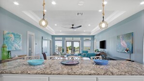 A spacious living room with a large island, a ceiling fan, and artwork on the walls. -  Private Heated Pool & Hot Tub ~ Ocean View ~ King Beds ~ Quiet & Peaceful (Bolivar Peninsula)