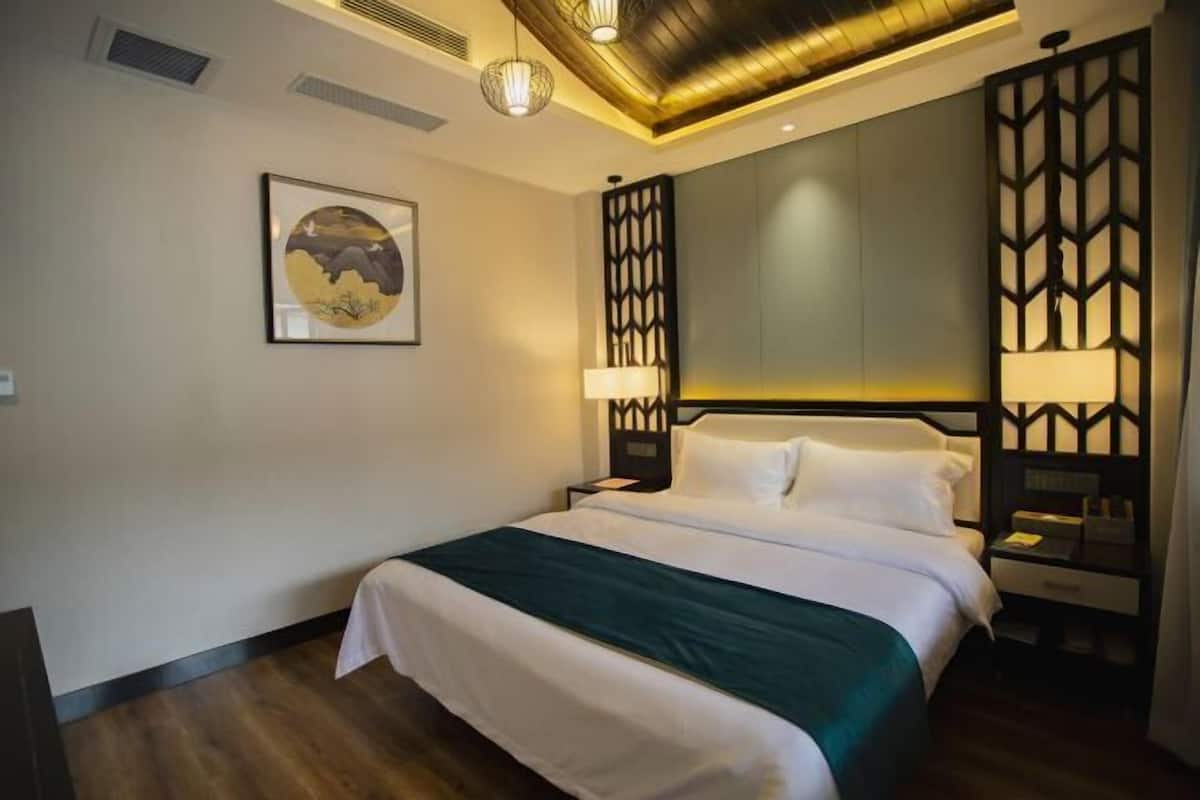 A hotel room with a bed, bedside lamps, a wall-mounted artwork, and a decorative panel.