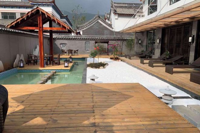 Un pati tradicional amb un pont de fusta, una petita piscina i una zona de seients amb coixins.