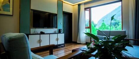 A modern living room with a sofa, a coffee table, a TV, and a large window with a view of greenery.