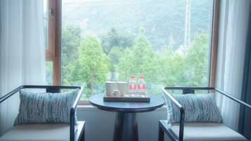A room with two chairs facing a window, a small table with a tray of items, and a view of a forested area.