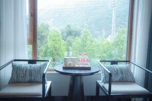 Una habitación con dos sillas mirando a una ventana, una mesita con una bandeja de objetos y vistas a un área boscosa.
