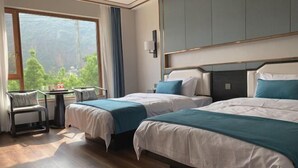 Een hotelkamer met twee bedden, een kleine tafel, een stoel en een groot raam met uitzicht op groen.